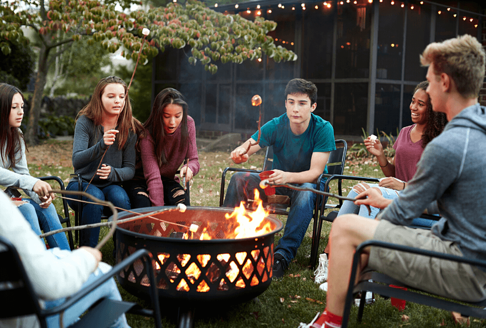 Group of young people toasting marshmallows over a fire pit