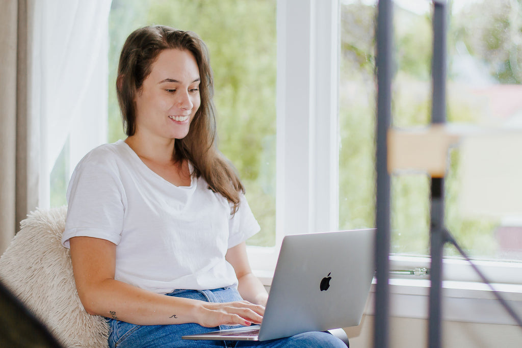 Taylor Pahuru sitting at a bay widow with laptop. Taputapu Graphic Designer