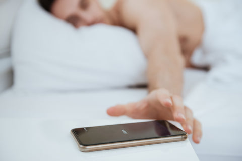 cropped-image-of-man-lying-on-bed-and-pulling-to-the-phone-which-lying-near-the-bed