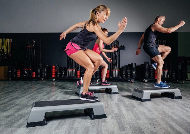 Woman trainer doing aerobic class with steppers in gym