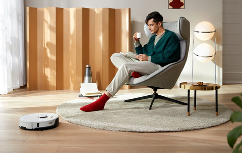 A white S8 Pro Ultra vacuuming a carpet while a man enjoys coffee nearby.