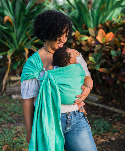 image of person of color wearing a baby in a mint Studio Tekhni ring sling baby carrier