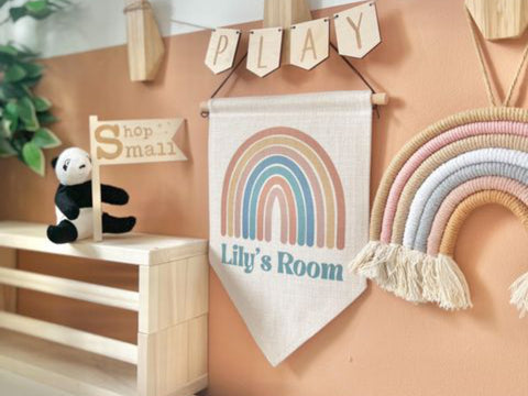 Canvas banner with rainbow and child's name on it next to a neutral coloured woven rainbow