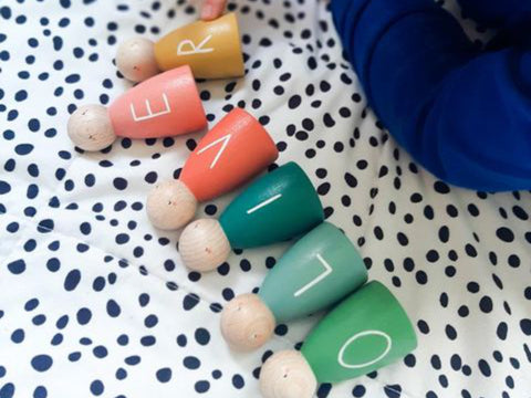 six wooden peg dolls in a range of colours each with a letter on it being played with by a child.