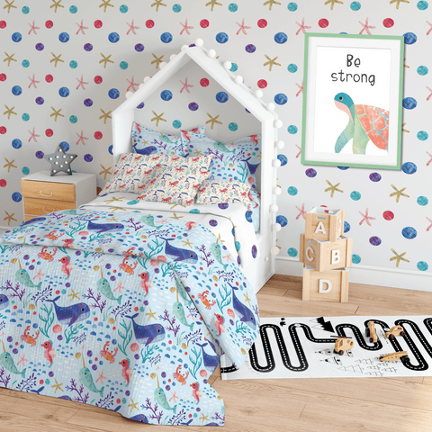 A childrens bedroom sceme showcasing various sea themed patterns including wallpaper and a blue duvet set. Also a be strong turtle print hanging on the wall.
