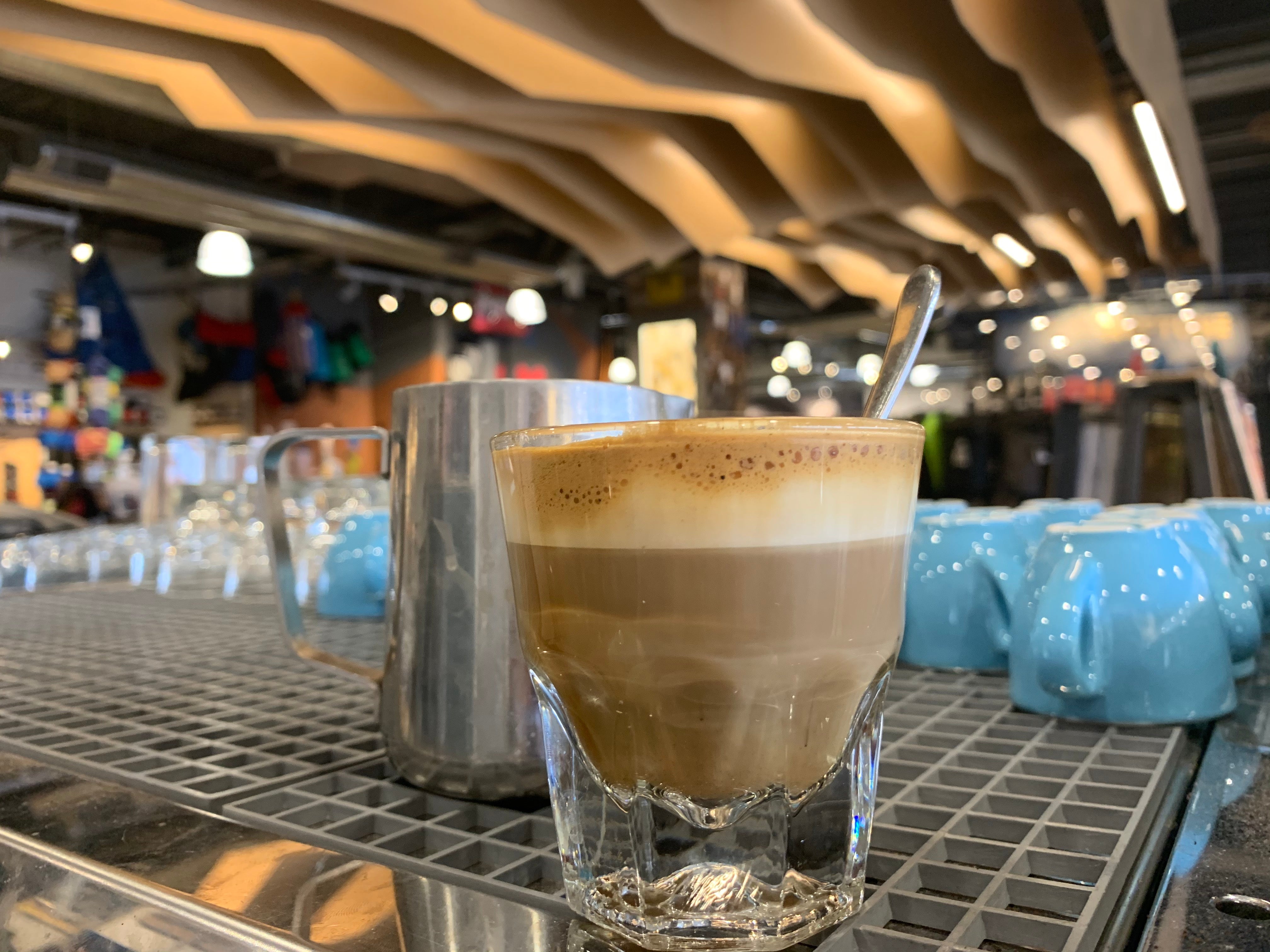 An image of an espresso shot with milk, with small blue espresso mugs, glassware, and the Neptune Cafe in the background