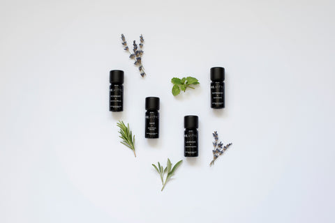 4 organic essential oils and plants laid on a plain light background