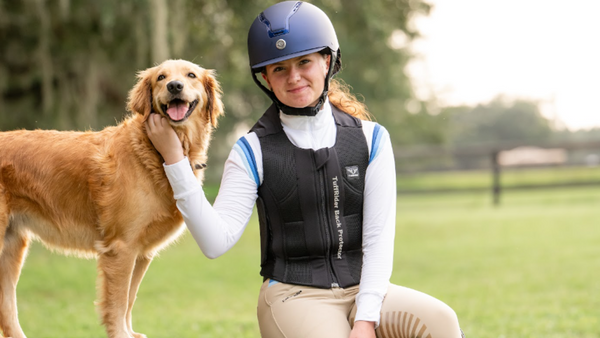 girl wearing english horse show clothes and golden retriever sitting on a log