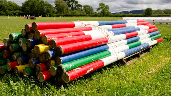 a pile of poles of different colors sits on the ground, waiting to be used in ground work exercises for horses