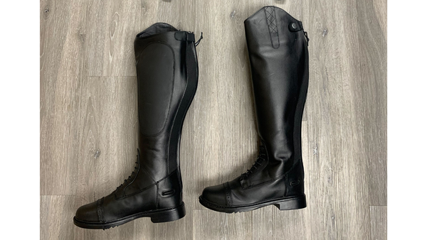 plus size equestrian tall boots, black leather riding tall boots against a dark grey wood floor. Plus size equestrian clothing. 