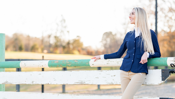 blond woman wearing english horse show clothes leaning up against a show jumping fence