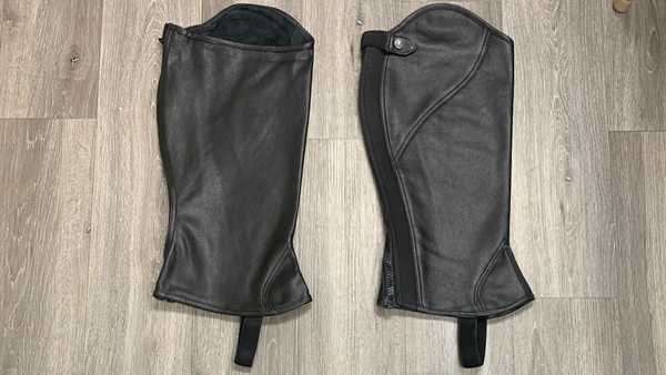 plus size black leather half chaps laid out on a grey wood floor. Plus size equestrian clothing