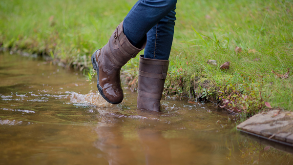 horse riding safety gear includes footwear. Legs wearing brown muck boots walking through a stream
