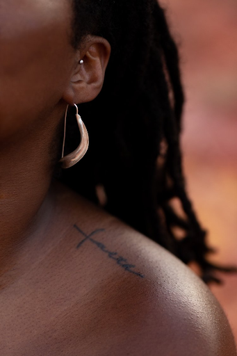Black woman wearing ear rings and a tattoo on her shoulder
