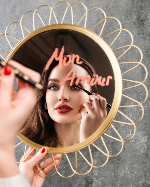 Woman applying the Feutre Fin eyeliner in a mirror with the words "Mon Amour" 