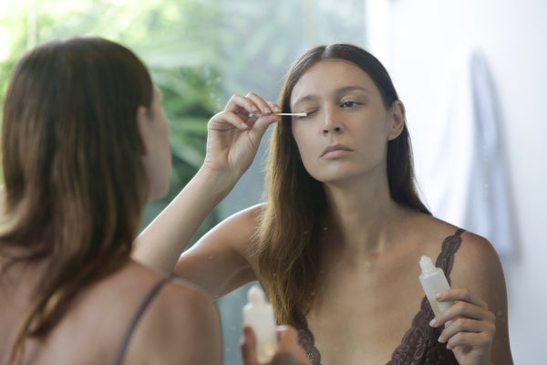 Woman applying serum for eyelash growth in front of the mirror