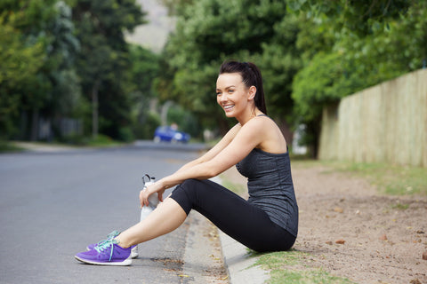 Woman sitting on side of road with water bottle in hand after finishing workout