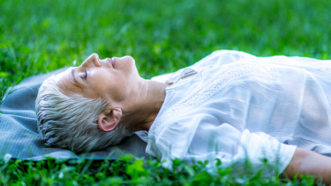 Older woman lying down on the grass meditating and relaxing