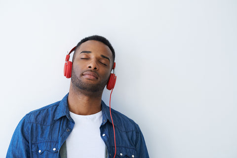 African American man leaning against a wall with red headphones listening to soothing music