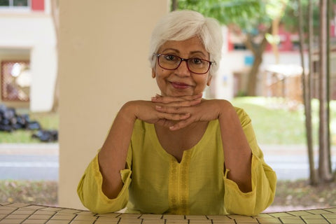 Old Indian Woman sitting at a table with fingers interlaced and her chin resting on her hands