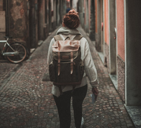 Woman walking with a backpack down an old brick paved European street