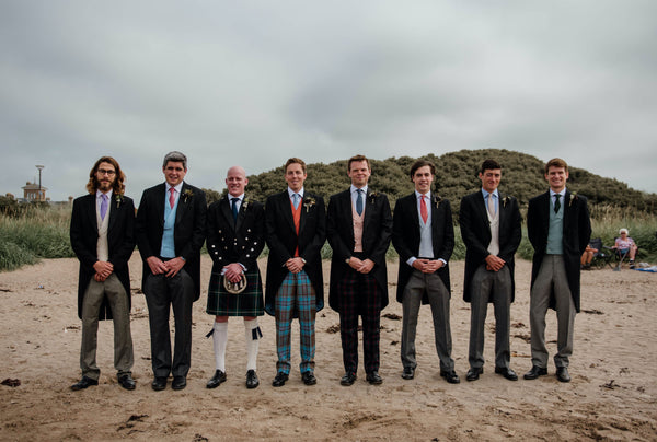 A groom in tartan trousers on the beach with his ushers