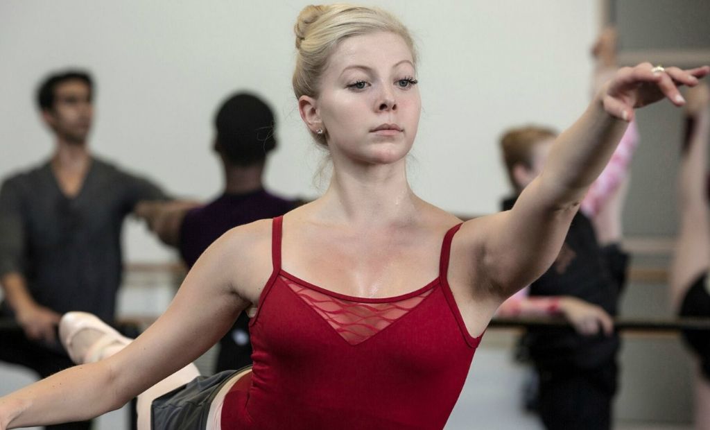 A female ballet dancer practising at the barre in the classroom with help from her teacher