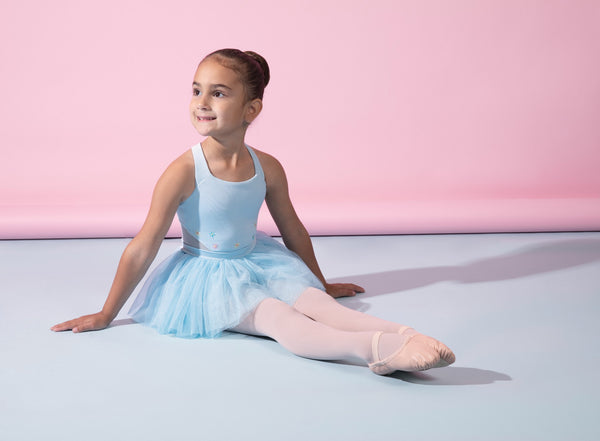 A young ballet dancer sitting on the floor in a blue tutu