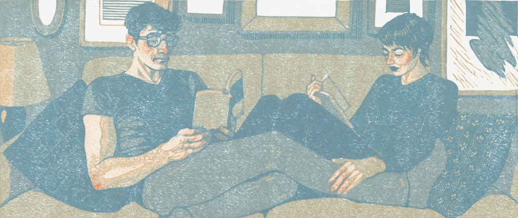 Quarantine Romance: a linocut print in gray and blue of two people reading on a couch.