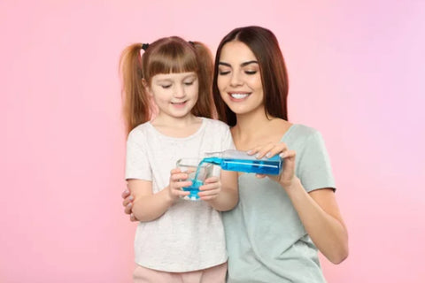 a little girl using mouthwash with her mom