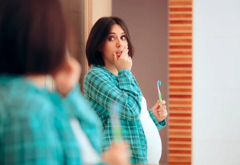 a pregnant woman with toothbrush in front of the mirror