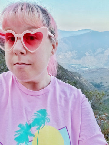 pink haired woman with heart sunglasses posing in front of a canyon.