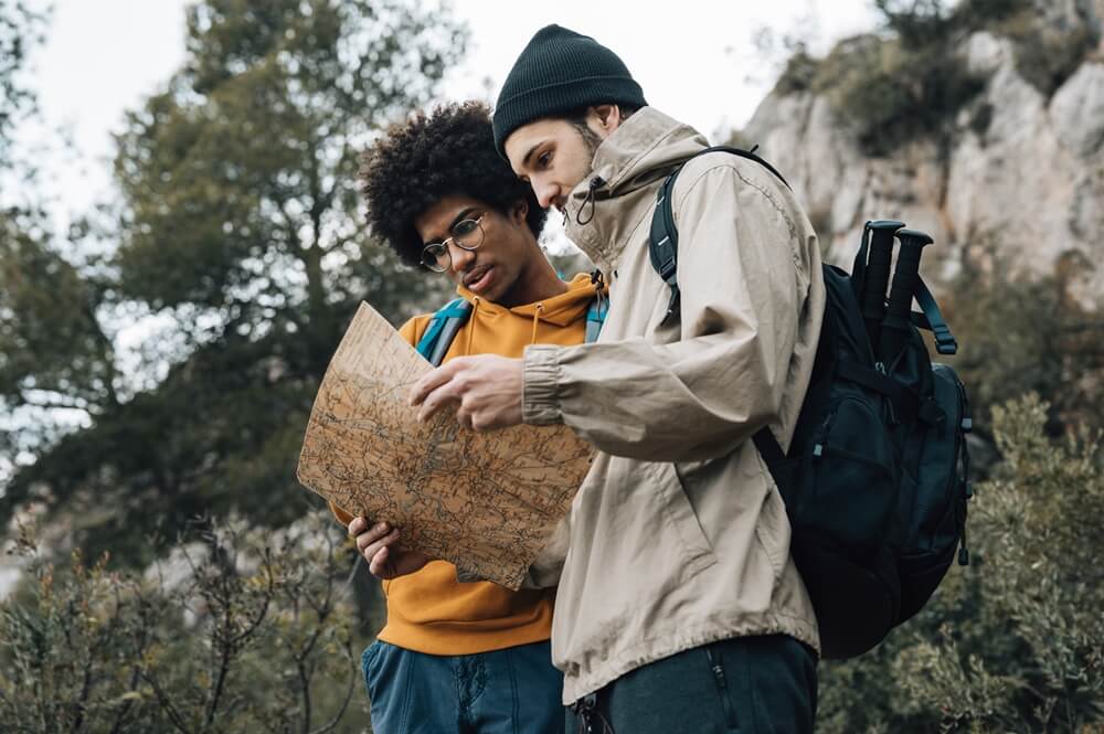 low-angle view sustainable travelers reading a map while hiking with eco-friendly travel bags