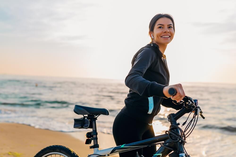smiling young woman riding a bicycle in morning sunrise on a beach