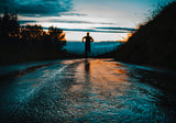 a shadowed person is running on an empty road with a sunset in the background 