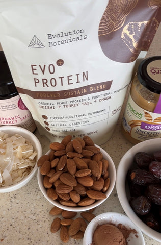 Ingredients needed for gut friendly chocolate peanut butter protein balls sitting on a marble table, including: almonds, dates, cacao and peanut butter.
