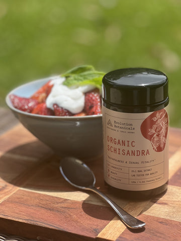 A jar of Evolution Botanicals' Organic Schisandra sitting next to a bowl of strawberries and a spoon on a wooden table.