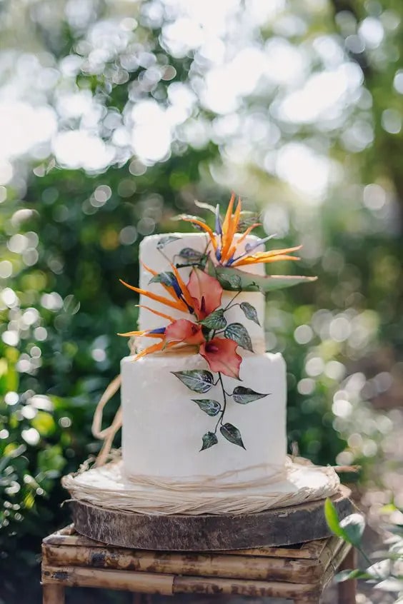 A white wedding cake adorned with tropical flowers.