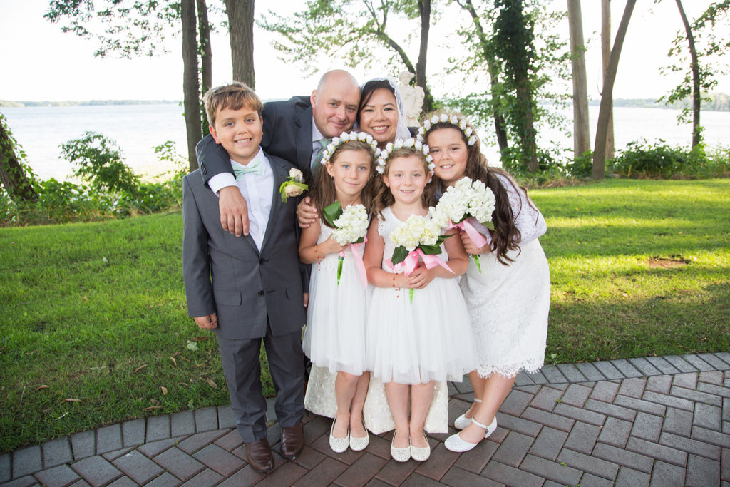 Groom with three flower girls dressed in white with a flower boy pose outdoors during a charming and intimate Filipino and Italian intercultural wedding in Canada.