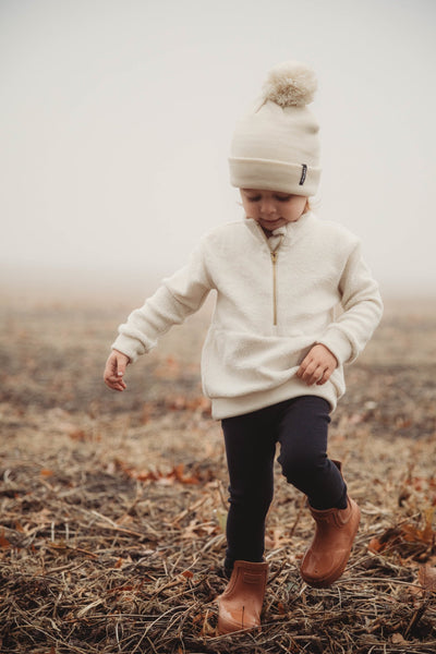 boy wearing white half zip sweater black pants and white beanie