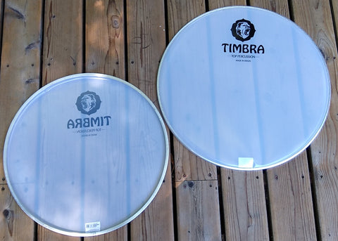 White plastic surdo head, translucent drum heads on wooden porch. Timbra logo visible.
