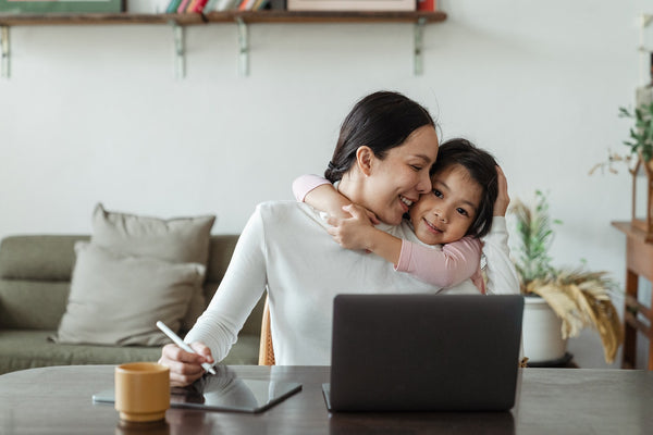 A woman happily working from home with her daughter