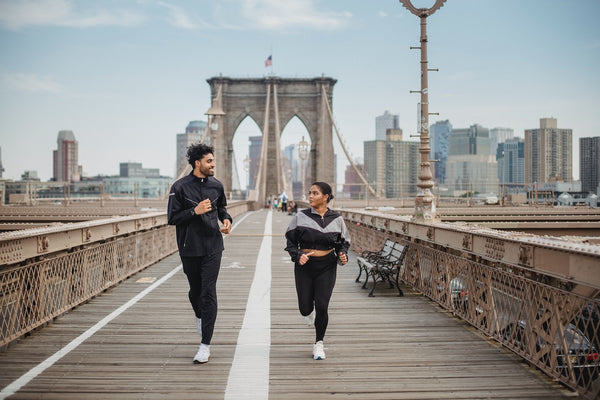 A young couple running across the Brooklyn Bridge