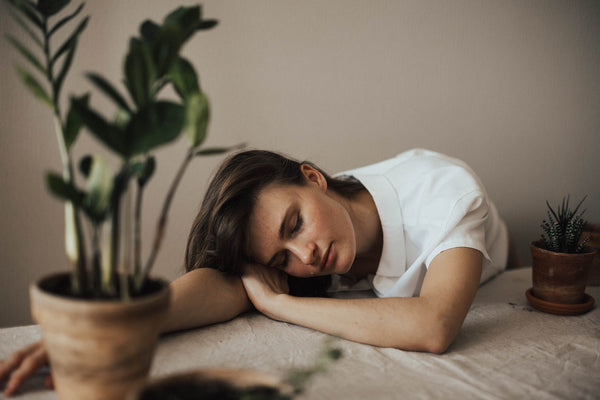 an exhausted woman wearing white laying on her desk with her head down