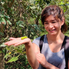Founder, Lily at the peace silk farm with silkworm in palm of hand, India