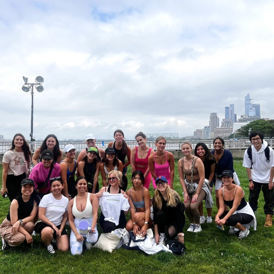 A large group of people posing together outdoors in a park with a cityscape in the background.