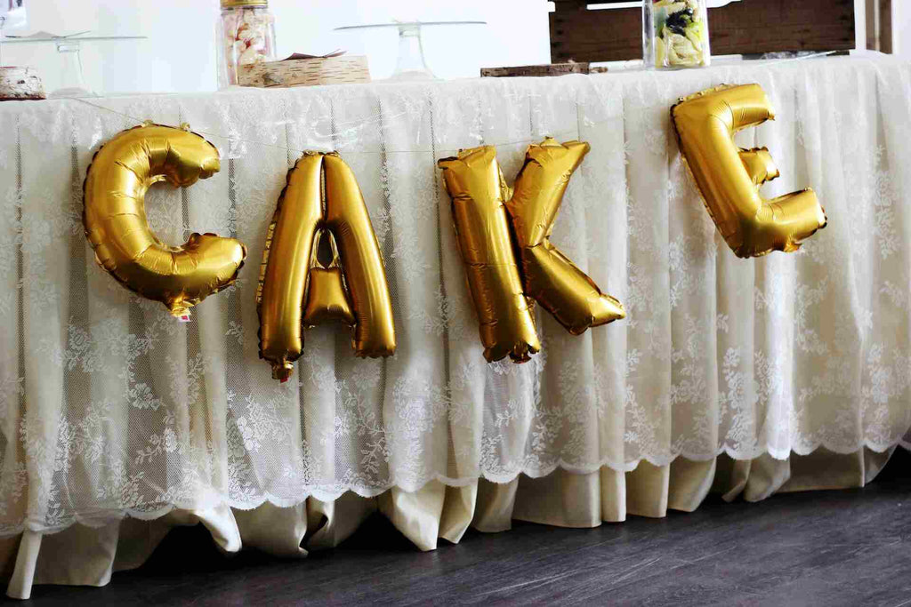Gold balloons spelling cake on a white table