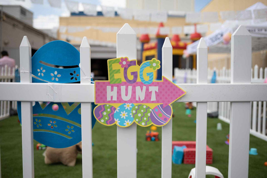 An egg hunt sign hanging on a white picket fence