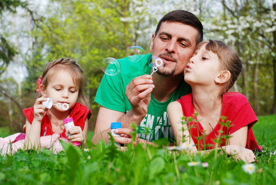 A man is enjoying Father’s Day activities while blowing bubbles with his children.