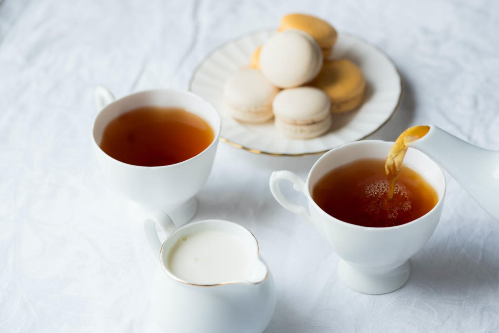 Pouring tea in a mug next to macarons and a pitcher of milk